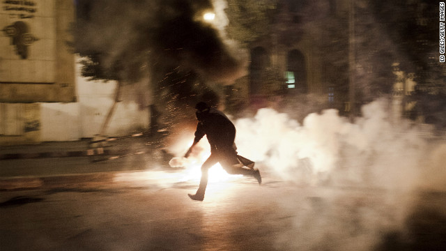 催涙ガスの筒を手に走るデモ参加者＝２６日、カイロ