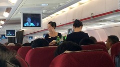 軽食を提供する高麗航空の客室乗務員。モニターに映っているのはテレビ中継された北朝鮮のコンサートで、主に軍隊に関する愛国的な歌を流している