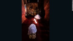 教会で聖ゲオルギウスのタペストリーの前にひれ伏す巡礼者ら。床には窓から流れ込んだ光により十字架が映し出されている