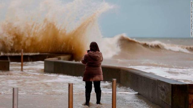 フランス北西部で防潮堤に打ちつける波を写真に収める女性