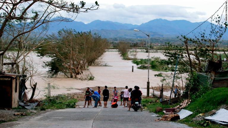 水に沈んだ道路の横に立つ住民＝１５日、フィリピン・トゥゲガラオ/Aaron Favila/AP