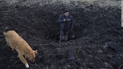 ウクライナ・タマルチュクで自宅裏の畑への砲撃であいた穴の大きさを示す男性＝２０日