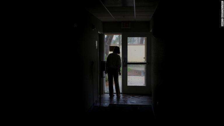 停電が発生し、ドアから被害状況を見る女性＝２８日、米フロリダ州フォートマイヤーズ/Marco Bello/Reuters