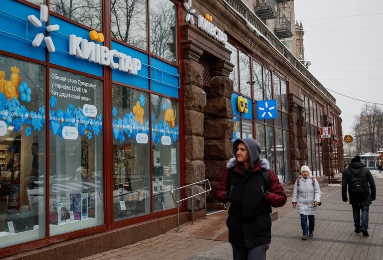 ウクライナの通信会社キーウスターの店舗前を通り過ぎる人々＝１２日、ウクライナ・キーウ/Alina Smutko/Reuters