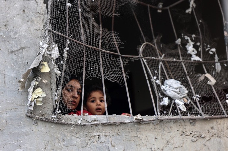 イスラエルによる爆撃で被害を受けた建物の窓から外を眺める女性と子ども＝２０２３年１１月、パレスチナ自治区ガザ地区ラファ/Said Khatib/AFP/Getty Images