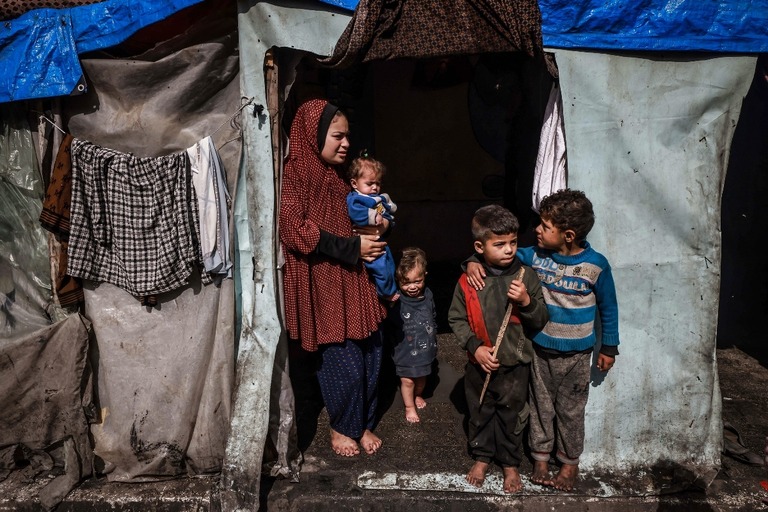 住む土地を離れ避難したパレスチナ人の女性と子どもが急ごしらえのテントの入り口に立つ＝３月１４日、ラファ/Mohammed Abed/AFP/Getty Images