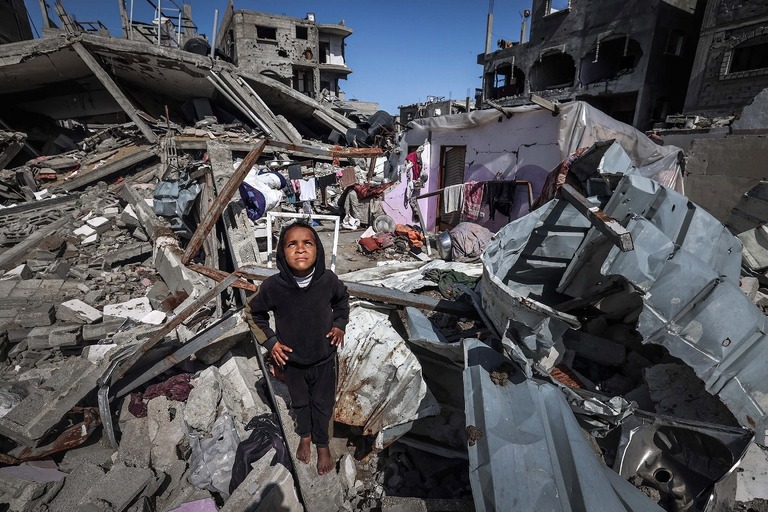 ラファ難民キャンプで瓦礫の中から上空の軍用ドローンを見上げるパレスチナ人の少女/Mohammed Abed/AFP/Getty Images
