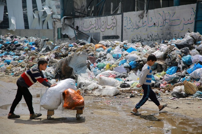 ゴミの山の前を通る子ども＝３月２８日、パレスチナ自治区ガザ地区/AFP/Getty Images