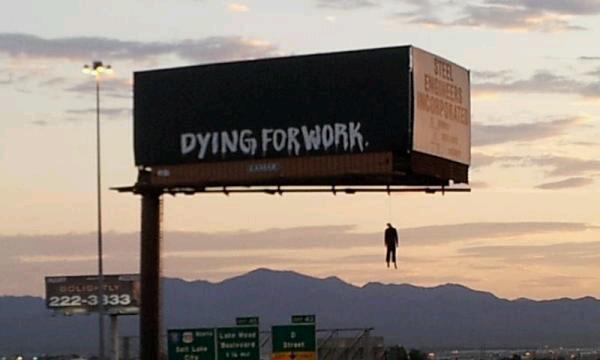 「Ｄｙｉｎｇ　ｆｏｒ　ｗｏｒｋ（死ぬほど仕事がしたい）」の文字の下にビジネススーツを着せられロープでつり下げられたマネキン