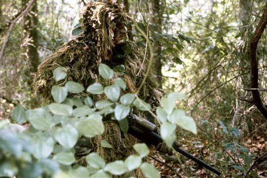 写真は、落ち葉や草に似せた「ギリースーツ」と呼ばれる迷彩服を着た海兵隊スナイパー　(C)DOD