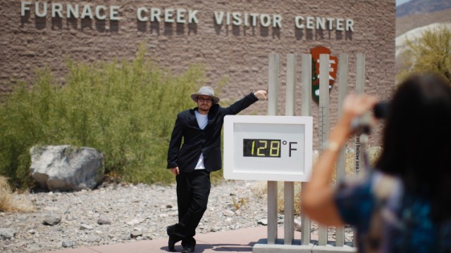 記録的猛暑を示した温度計の横で記念写真をとる男性