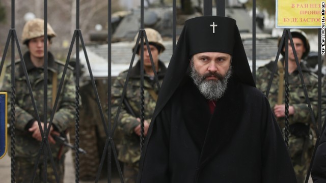 ロシア語を話す兵士数百人に囲まれたウクライナ軍基地の門前に立つ聖職者＝２日