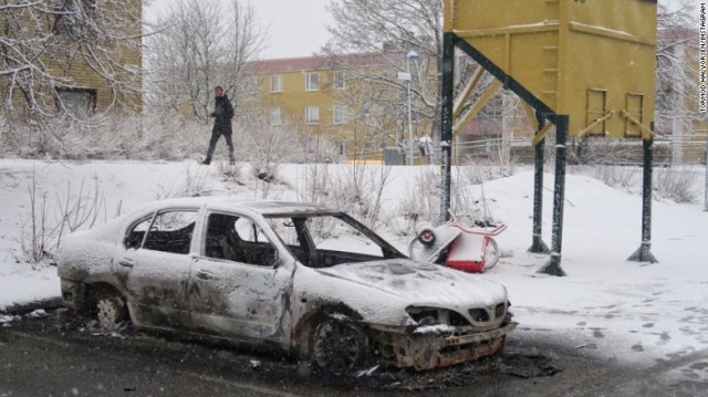 暴動で放火された車を調べる警察官