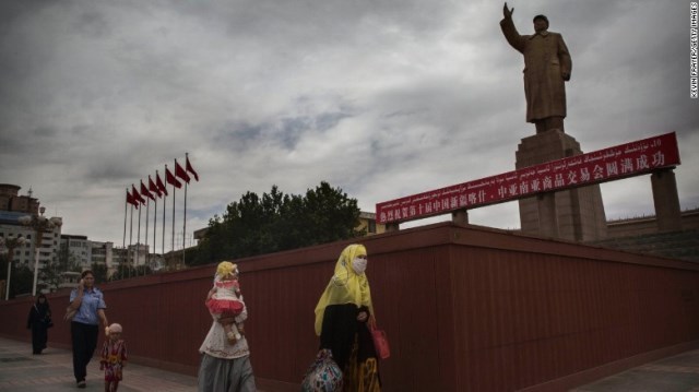 ベールで顔を隠した女性が毛沢東の像の前を歩く＝１４年７月、カシュガル