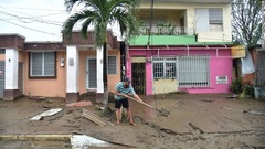 プエルトリコのトア・バハで泥だらけになった道を清掃する男性 