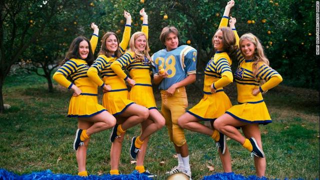 UCLAのフットボールのユニホームを着て、チアリーダーとともにポーズ
