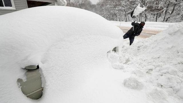 ペンシルベニア州エリーで車に降り積もった雪をかく男性