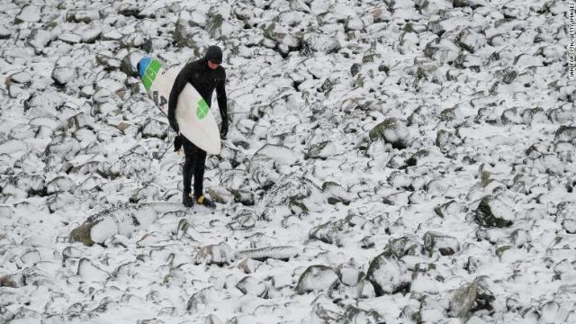 北東イングランドのレッドカーで凍った岩の上を歩くサーファー