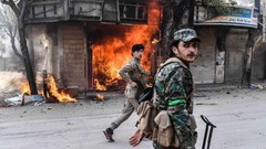 火をつけられた店舗の前を歩く反体制派の兵士