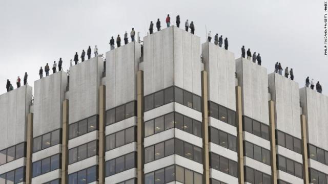 ビル屋上の縁にずらりと並び立つ８４体の彫像。自殺した男性を表している