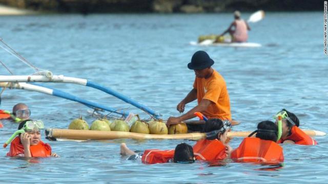 サーフボードに乗って海水浴客にココナッツのジュースを売る男性