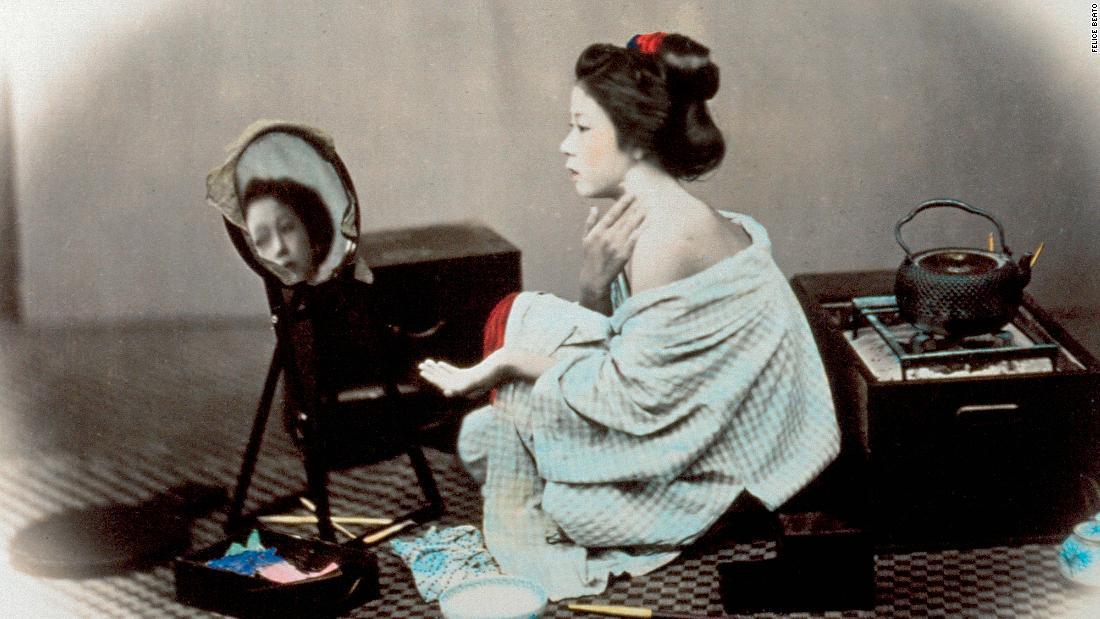 片方の肩を見せて白い化粧をする女性。官能的な画像は19世紀末に多くの旅行客を日本に呼び寄せた=Felice Beato