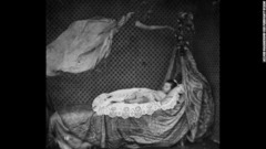 ベッドで眠る赤ちゃんの上を幽霊のような人物が漂っている