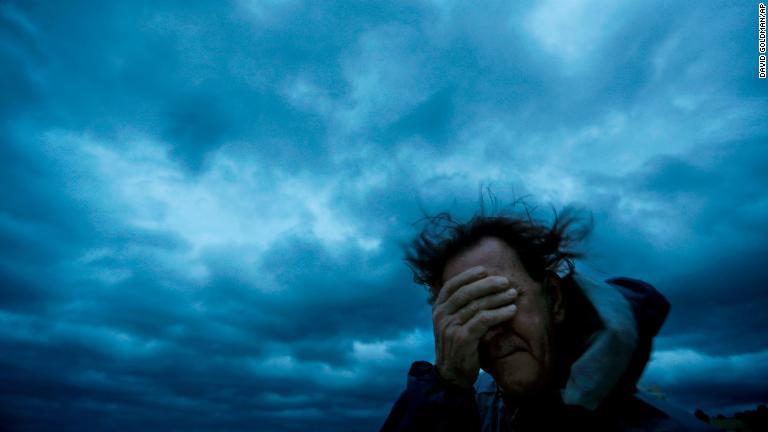 風と砂で目をふさぐ女性＝１４日、ノースカロライナ州マートルビーチ/David Goldman/AP