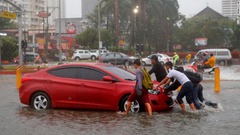 水にはまった車を押す人たち＝１５日、マニラ