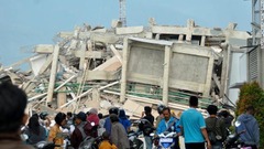 地震で倒壊した建物の周りに集まった住人ら＝２９日、パル市