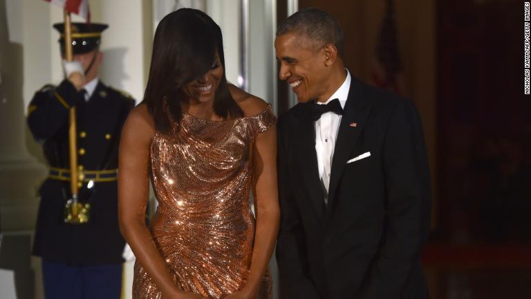 ヴェルサーチェのきらめくドレスを身にまとったミシェル・オバマ前米大統領夫人。隣にはオバマ前大統領の姿も/NICHOLAS KAMM/AFP/Getty Images