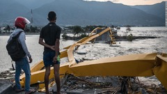 地震や津波によって壊れた橋を見る男性ら