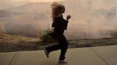 消防隊員が消火作業に当たるなか、避難する女性＝１０日、カリフォルニア州カラバサス