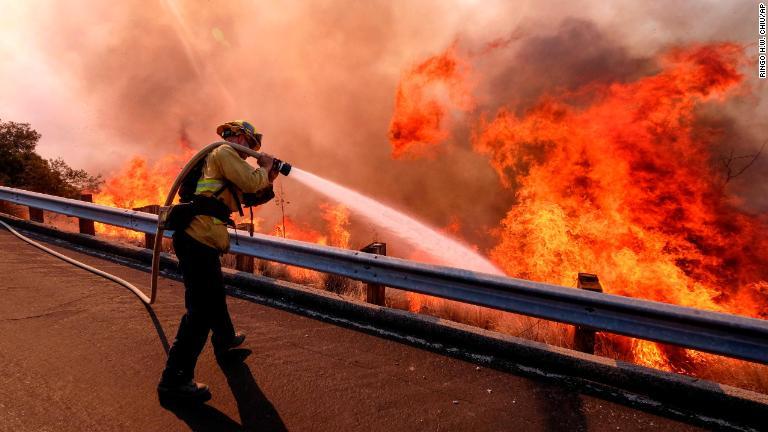 高速道路から放水する消防隊員＝１２日、カリフォルニア州シミバレー/Ringo H.W. Chiu/AP