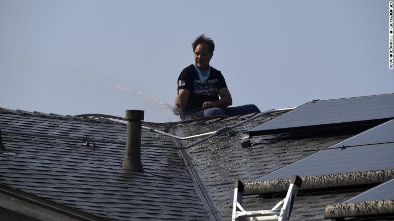自宅の屋根を水で洗い流す男性＝１２日、カリフォルニア州シミバレー/Kevork Djansezian/Getty Images