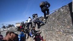 米・メキシコ国境へ向かおうとフェンスを乗り越える人々