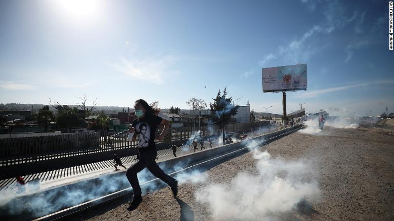 顔を覆って催涙ガスから逃げる移民の男性/Hannah McKay/REUTERS