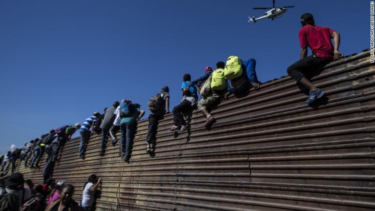鉄製のフェンスを乗り越える移民ら＝２５日、メキシコ・ティフアナ/Pedro Pardo/AFP/Getty Images