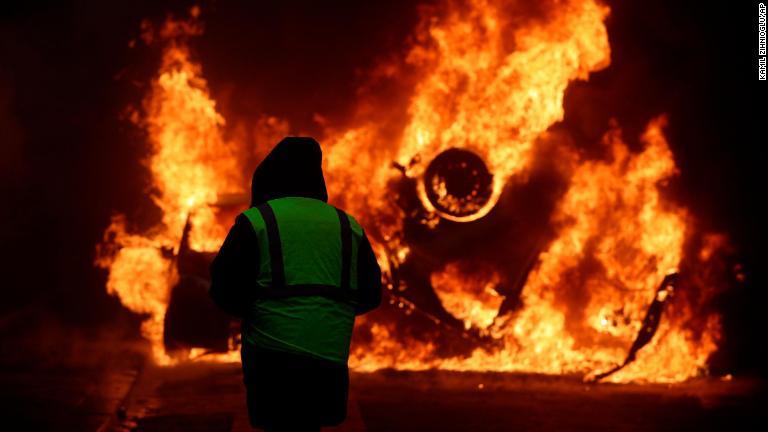 燃え盛る車両を眺めるデモ参加者/Kamil Zihnioglu/AP