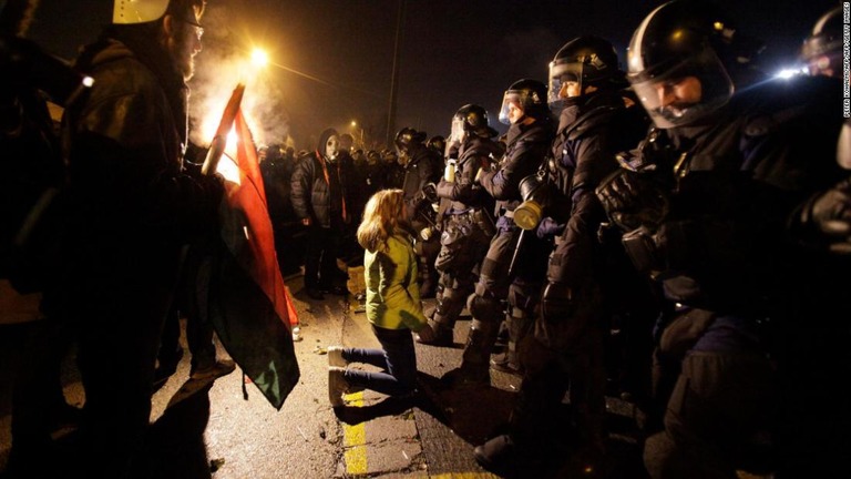 国営テレビの本社前でひざをついて警官隊に対峙するデモ参加者/PETER KOHALMI/AFP/AFP/Getty Images