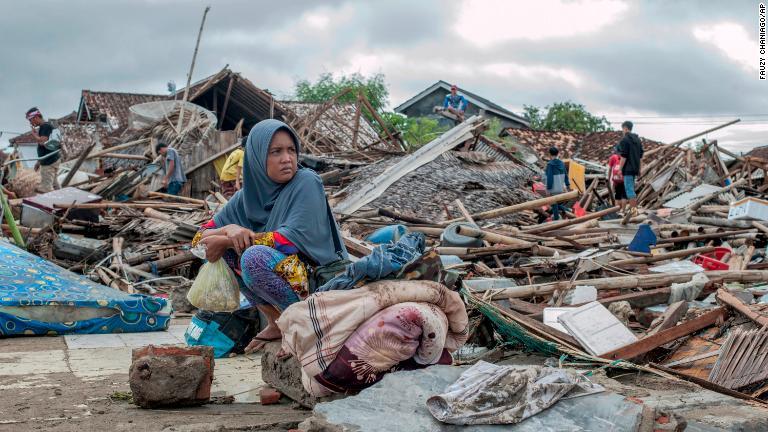 破壊された家屋から使えるものを回収して座り込む女性/Fauzy Chaniago/AP