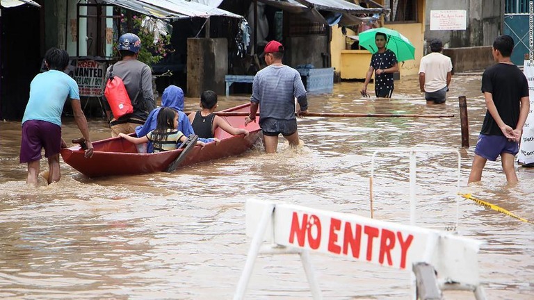 冠水した道路をボートなどで移動する人たち＝フィリピン南カマリネス州/SIMVALE SAYAT/AFP/Getty Images