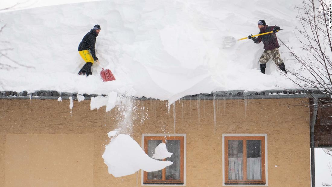 男性2人が住宅の屋根から雪を取り除こうとする様子=オーストリア/CHRISTIAN BRUNA/EPA-EFE