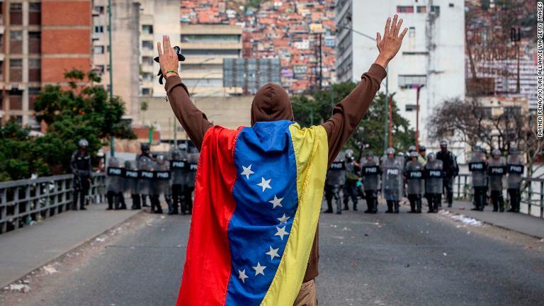 ベネズエラ国旗をみにまとって治安部隊と対峙する男性＝１月２３日、首都カラカス/Rayner Pena/picture alliance via Getty Images