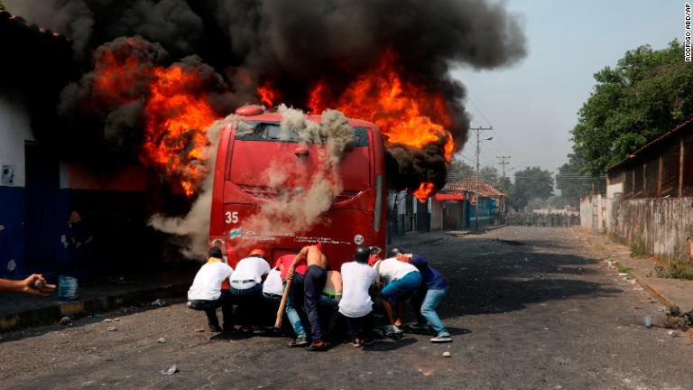 出火したバスを押すデモ参加者＝２３日、ベネズエラ・ウレニャ/Rodrigo Abd/AP