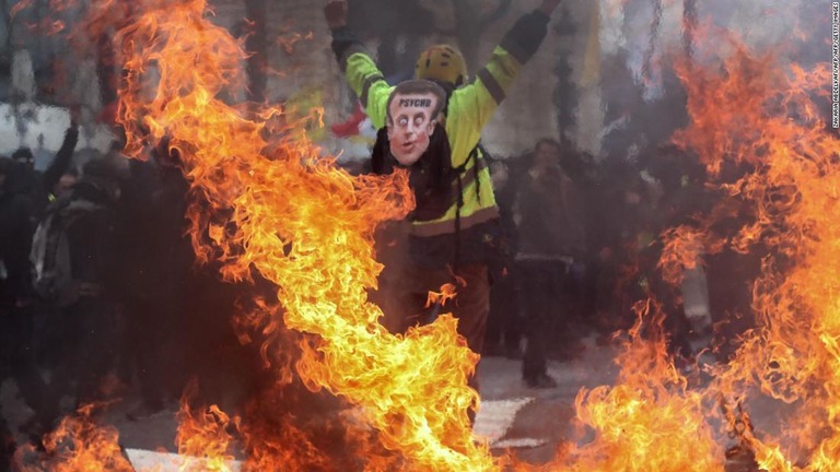 マクロン大統領に似せたマスクを背負って燃えるバリケードの近くに立つデモ参加者＝１６日/ZAKARIA ABDELKAFI/AFP/AFP/Getty Images
