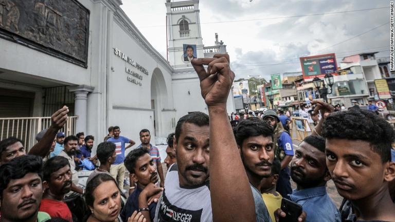 聖アンソニー教会の前で血の付いた写真を掲げる男性/Tharaka Basnayaka/Getty Images