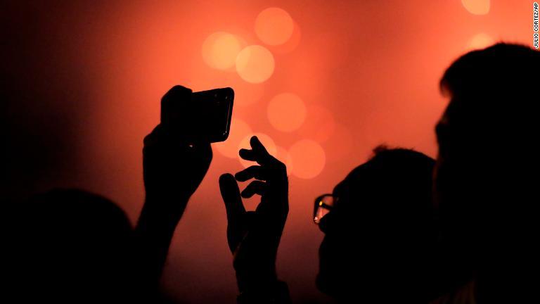 ボルチモアでの花火イベントで、携帯電話のカメラを操作する男性/Julio Cortez/AP