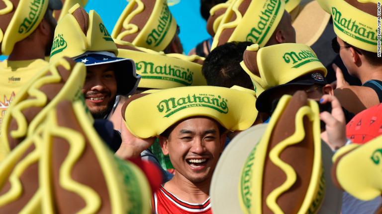 ホットドッグ早食い選手権を楽しむ人々。ホットドッグをデザインした帽子をかぶっている＝ニューヨーク/Anthony Behar/Sipa USA/AP