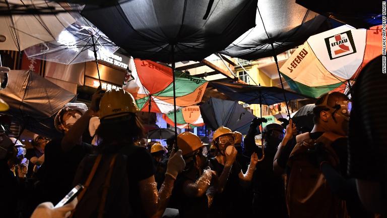 傘を使ってシェルターを作るデモ隊＝７月２８日/ANTHONY WALLACE/AFP/Getty Images